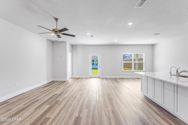 unfurnished living room with a textured ceiling, light wood-type flooring, ceiling fan, and sink