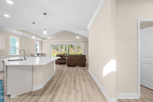 kitchen with a sink, white cabinetry, light wood-style floors, ornamental molding, and light stone countertops