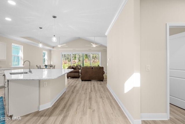kitchen with ornamental molding, light stone countertops, white cabinets, a sink, and light wood-style flooring