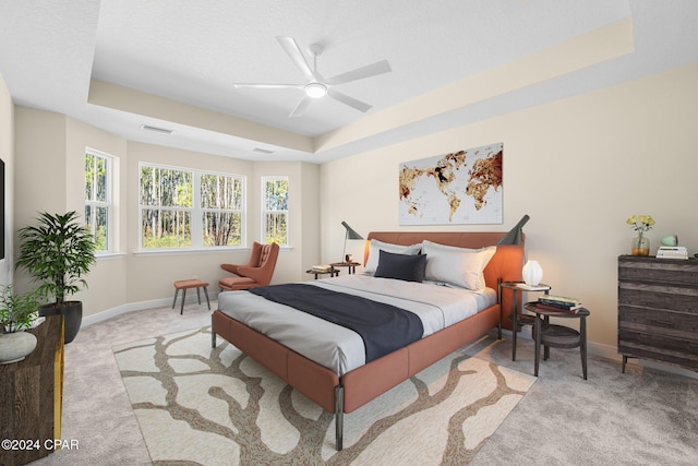 carpeted bedroom featuring a tray ceiling, baseboards, visible vents, and a ceiling fan