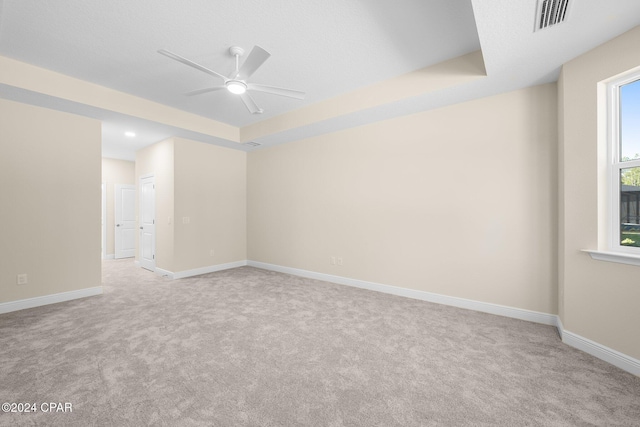 carpeted empty room with baseboards, ceiling fan, a raised ceiling, and visible vents
