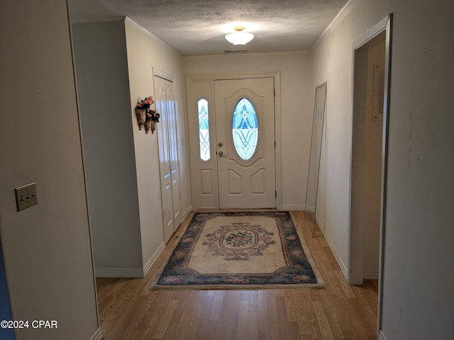 doorway to outside with ornamental molding, a textured ceiling, and light hardwood / wood-style flooring