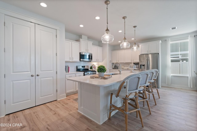 kitchen with stainless steel appliances, white cabinetry, a center island with sink, and light hardwood / wood-style floors