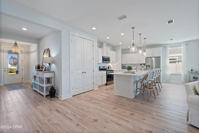 kitchen featuring light hardwood / wood-style flooring, pendant lighting, a kitchen island with sink, white cabinets, and appliances with stainless steel finishes