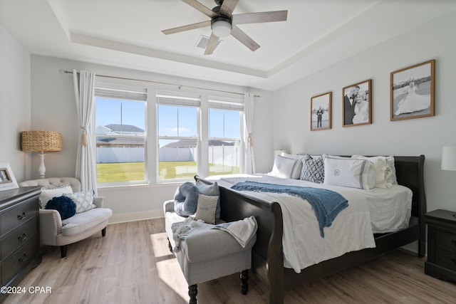 bedroom featuring a tray ceiling, light hardwood / wood-style flooring, ceiling fan, and a water view