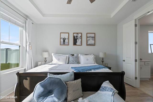 bedroom with a raised ceiling, multiple windows, ceiling fan, and hardwood / wood-style flooring