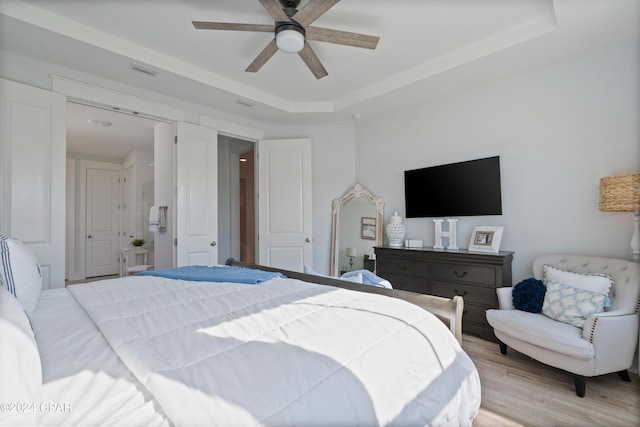 bedroom with ceiling fan, light hardwood / wood-style floors, and a tray ceiling