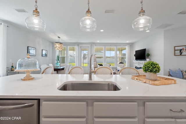 kitchen with light stone countertops, sink, an island with sink, and pendant lighting