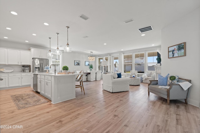 kitchen featuring appliances with stainless steel finishes, decorative light fixtures, a center island with sink, light hardwood / wood-style floors, and white cabinetry