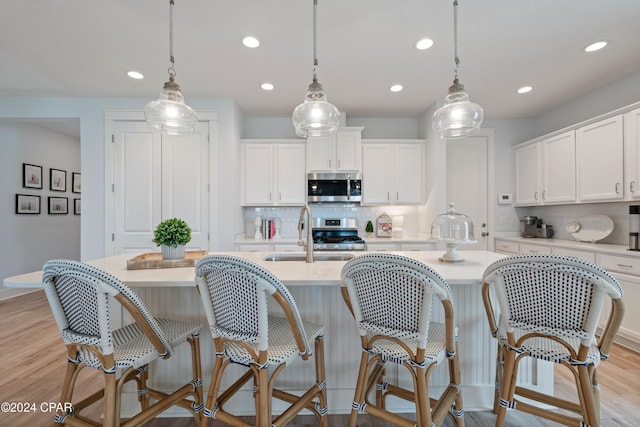 kitchen with pendant lighting, white cabinets, sink, light hardwood / wood-style flooring, and appliances with stainless steel finishes