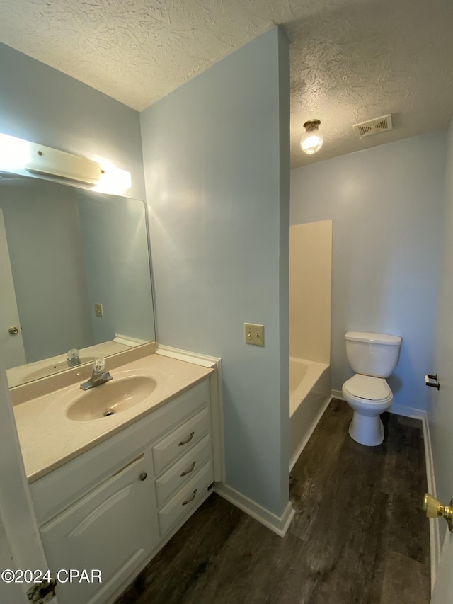 bathroom featuring a washtub, vanity, a textured ceiling, hardwood / wood-style floors, and toilet