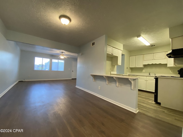 kitchen with a kitchen breakfast bar, ceiling fan, exhaust hood, dark hardwood / wood-style floors, and white cabinetry