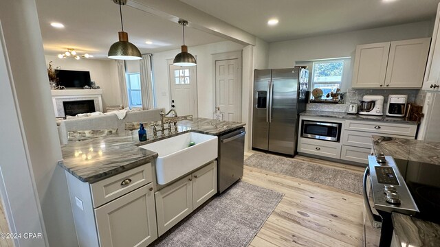 kitchen featuring sink, hanging light fixtures, stainless steel appliances, dark stone counters, and decorative backsplash