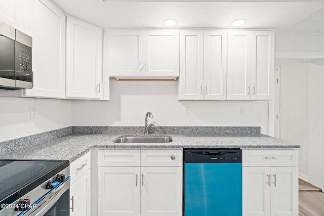 kitchen featuring sink, appliances with stainless steel finishes, light hardwood / wood-style floors, light stone counters, and white cabinetry