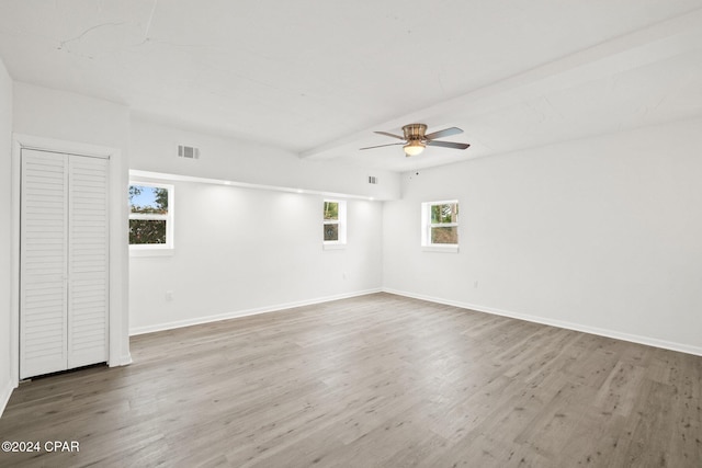 empty room featuring plenty of natural light, beamed ceiling, and hardwood / wood-style floors