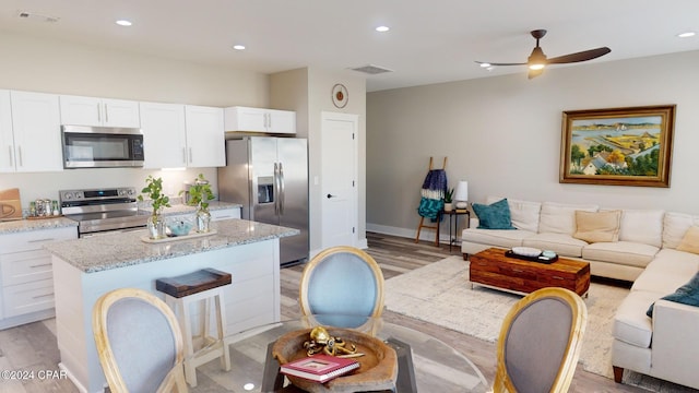 kitchen with white cabinets, appliances with stainless steel finishes, light hardwood / wood-style floors, and light stone countertops