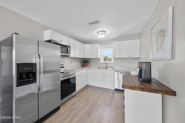 kitchen with stainless steel appliances, sink, white cabinets, light hardwood / wood-style floors, and butcher block counters