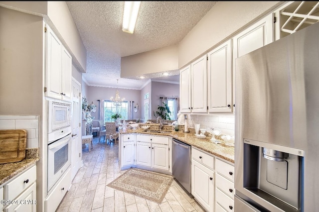 kitchen with kitchen peninsula, appliances with stainless steel finishes, a textured ceiling, sink, and white cabinetry