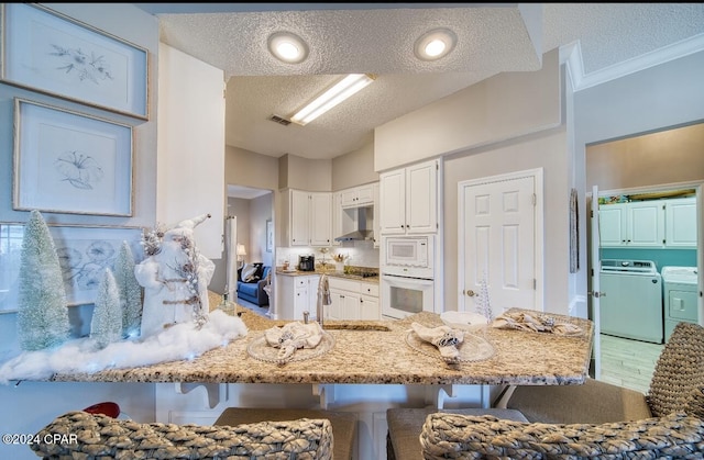 kitchen featuring kitchen peninsula, a kitchen breakfast bar, white appliances, white cabinets, and washing machine and dryer