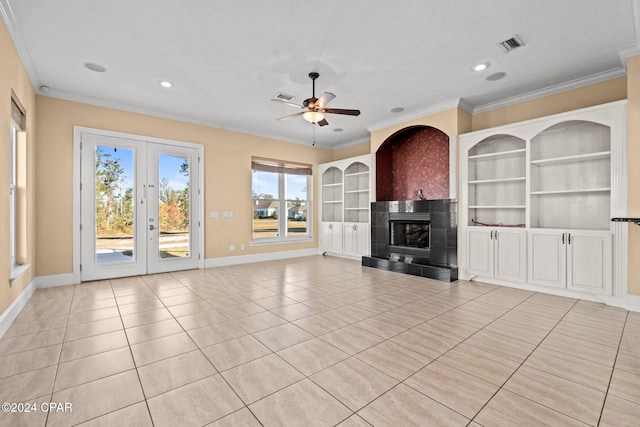 unfurnished living room with a tile fireplace, ceiling fan, built in shelves, ornamental molding, and light tile patterned flooring