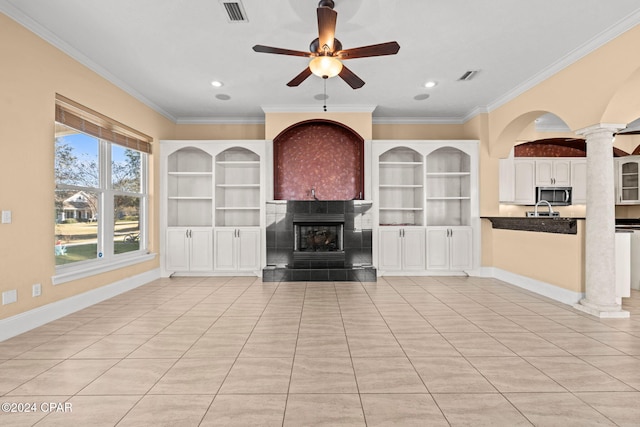 unfurnished living room featuring ornate columns, ceiling fan, crown molding, a tiled fireplace, and light tile patterned flooring