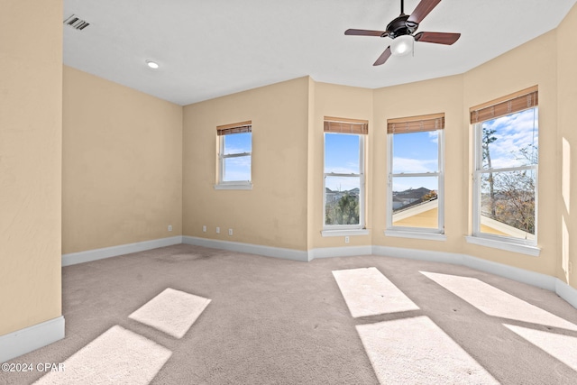 empty room with light colored carpet, a wealth of natural light, and ceiling fan