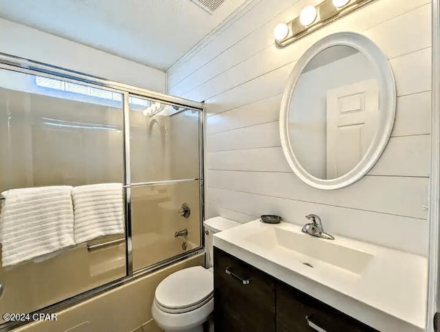 full bathroom with wooden walls, vanity, bath / shower combo with glass door, and toilet