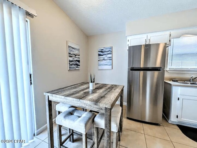 kitchen with light tile patterned floors, white cabinetry, a textured ceiling, and stainless steel refrigerator