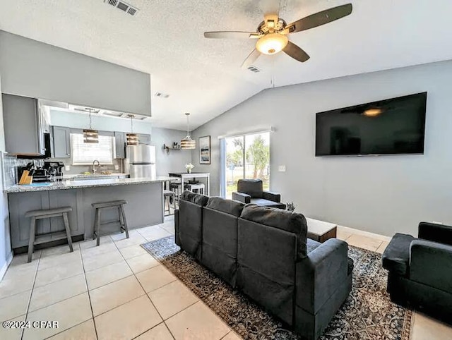 tiled living room with ceiling fan, sink, a textured ceiling, and vaulted ceiling