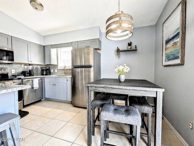 kitchen with backsplash, light stone countertops, light tile patterned floors, decorative light fixtures, and stainless steel appliances