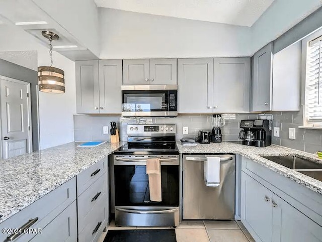 kitchen with light stone countertops, stainless steel appliances, vaulted ceiling, pendant lighting, and light tile patterned floors