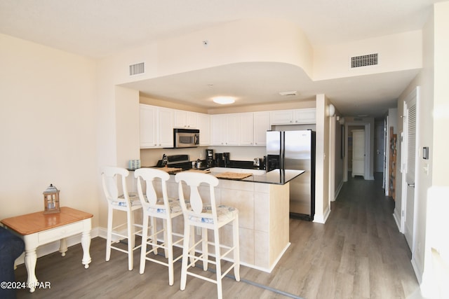 kitchen featuring kitchen peninsula, appliances with stainless steel finishes, light wood-type flooring, a breakfast bar, and white cabinets