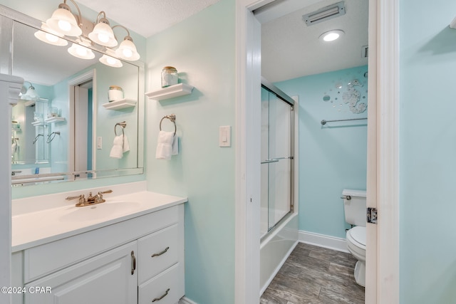 full bathroom featuring bath / shower combo with glass door, wood-type flooring, a textured ceiling, toilet, and vanity