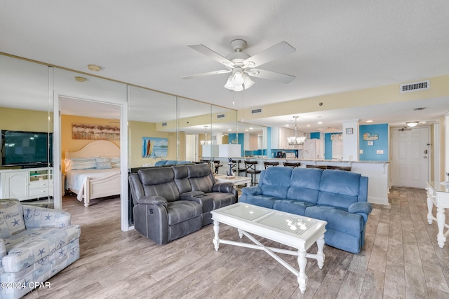 living room featuring ceiling fan with notable chandelier and light wood-type flooring