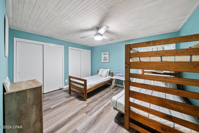 bedroom with ceiling fan, wooden ceiling, light hardwood / wood-style floors, and two closets