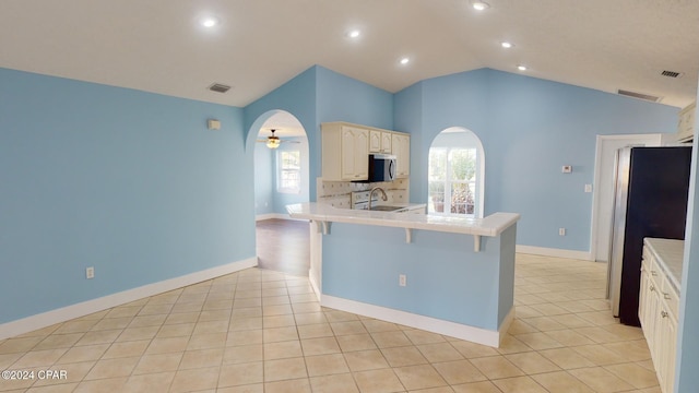 kitchen featuring kitchen peninsula, vaulted ceiling, a kitchen bar, white cabinetry, and stainless steel appliances