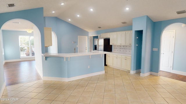 kitchen featuring stainless steel fridge with ice dispenser, light hardwood / wood-style flooring, vaulted ceiling, and a kitchen breakfast bar