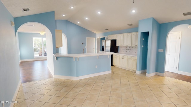 kitchen with backsplash, a breakfast bar, light hardwood / wood-style flooring, and vaulted ceiling