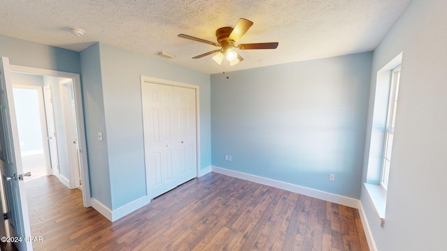 unfurnished bedroom with a textured ceiling, ceiling fan, dark wood-type flooring, and a closet