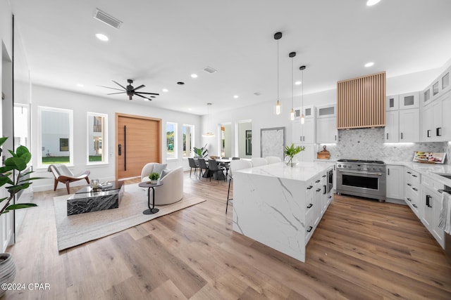 kitchen with range hood, high end stainless steel range, glass insert cabinets, open floor plan, and white cabinetry