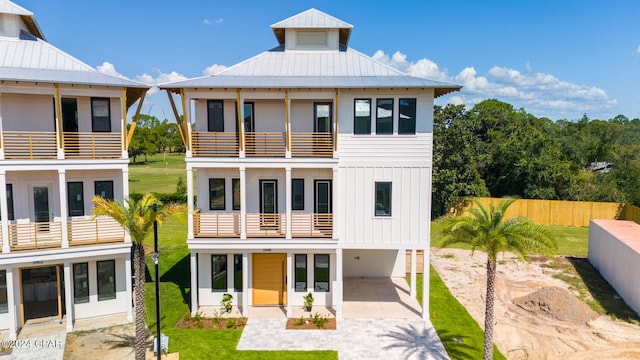 rear view of house with board and batten siding, a balcony, a standing seam roof, fence, and a carport