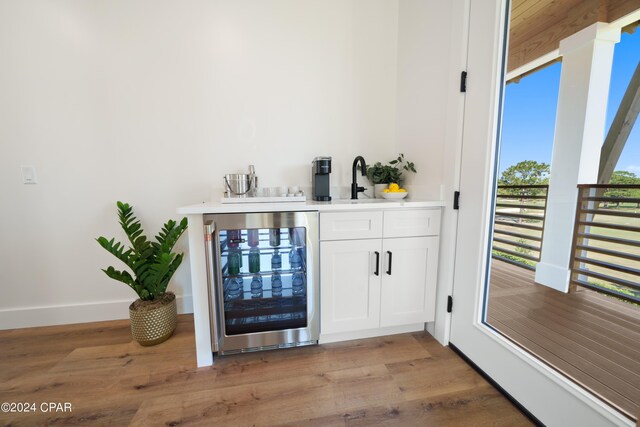 bar featuring light wood-type flooring, white cabinetry, sink, and beverage cooler