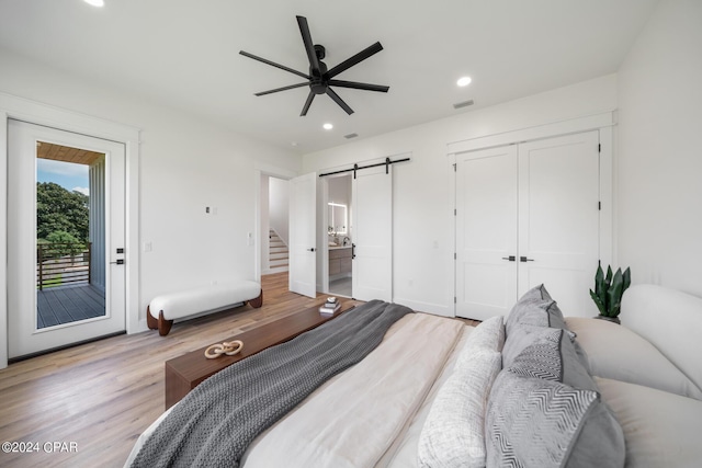 bedroom with connected bathroom, access to exterior, ceiling fan, a barn door, and light hardwood / wood-style floors