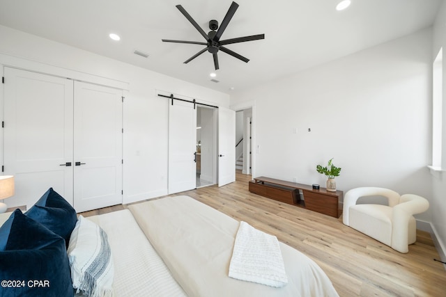 bedroom with a barn door, light hardwood / wood-style flooring, and ceiling fan