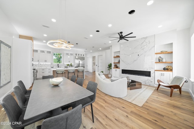 dining space featuring sink, ceiling fan, a premium fireplace, built in features, and light hardwood / wood-style floors