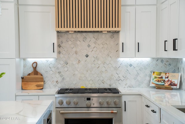 kitchen with light stone countertops, stainless steel range, tasteful backsplash, premium range hood, and white cabinets