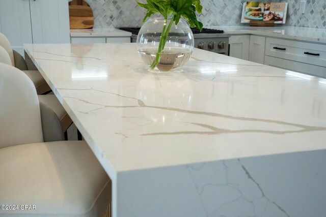 room details featuring light stone counters, white cabinetry, and backsplash