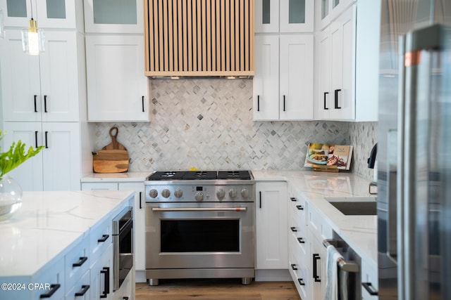 kitchen featuring light stone countertops, appliances with stainless steel finishes, decorative light fixtures, white cabinets, and hardwood / wood-style flooring