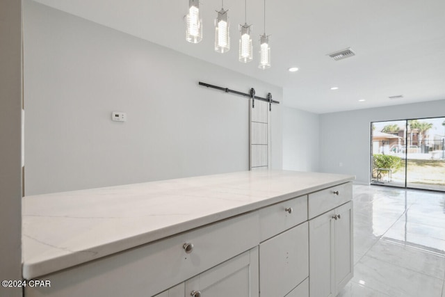 kitchen with white cabinets, pendant lighting, a barn door, and light stone counters