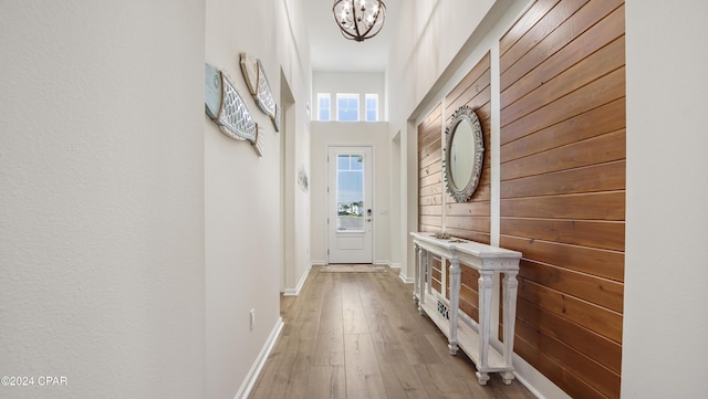 doorway featuring wood-type flooring, wooden walls, and a chandelier